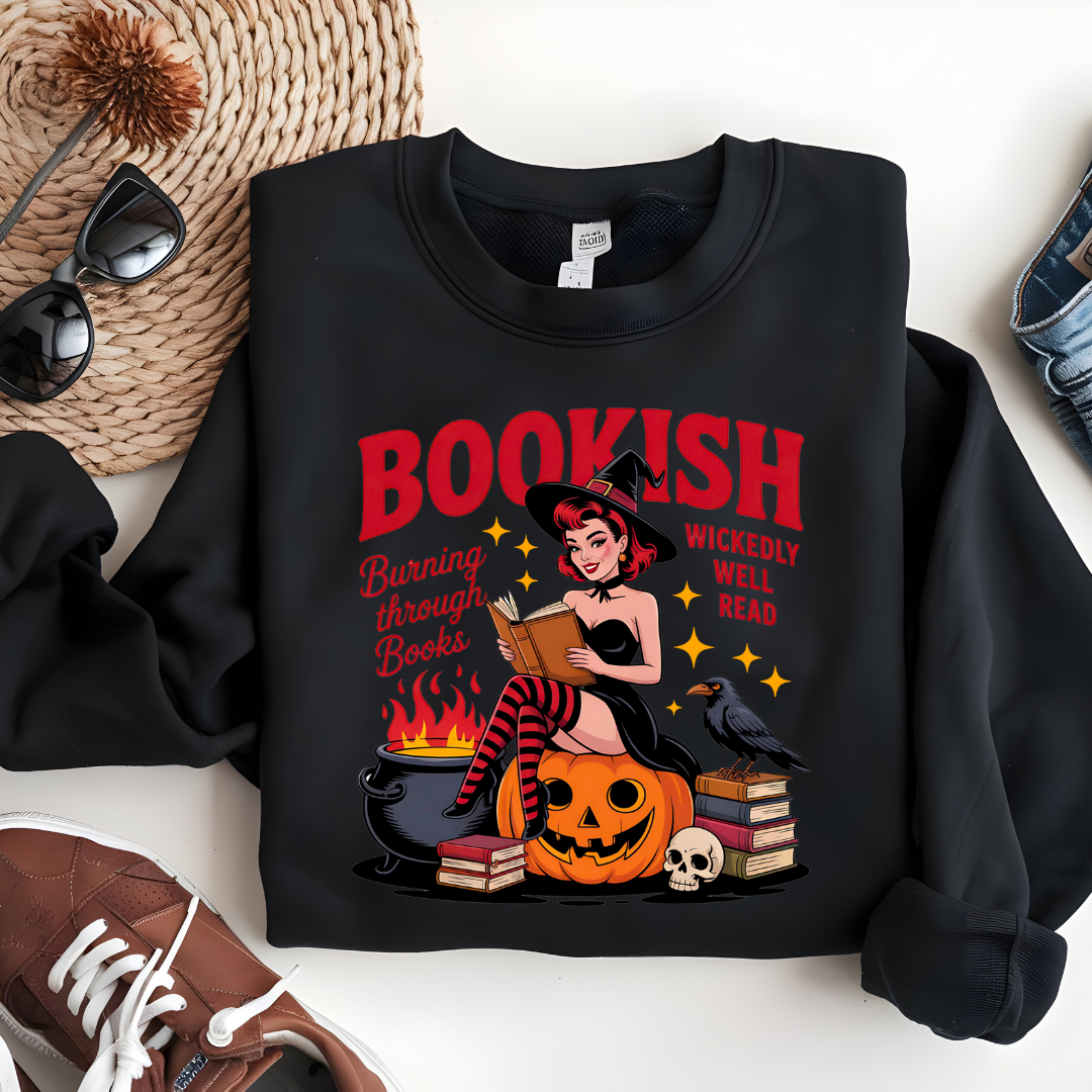 A flat lay of a black sweatshirt with Halloween-themed design featuring a witch, pumpkin and books by Fiction & Fibre.