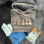A flat lay of a gray hoodie with cartoon ducks and the text bookish goose, socks, and a ghost figurine on a textured surface by Fiction & Fibre