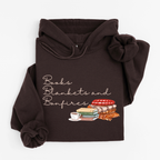 A dark brown hoodie laid flat on a light gray background, featuring a graphic print that reads 'Books Blankets and Bonfires' above an illustration of stacked books, a cup of tea, and cozy blankets.