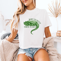 A woman wearing a white boxy crop that reads "Born to quest forced to rest" and has a sleeping dragon