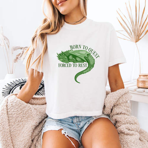 A woman wearing a white boxy crop that reads "Born to quest forced to rest" and has a sleeping dragon