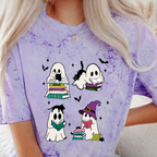 A person wearing a light purple tie-dye t-shirt with a cartoon graphic of four ghosts reading books in a Halloween theme. The person has blonde hair and is wearing a necklace.