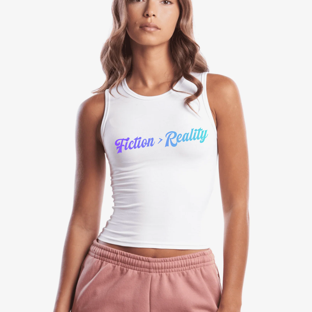A woman wearing a white sleeveless crop tank top with the text 'Fiction > Reality' printed across the chest in a blue-to-purple gradient, paired with dusty pink sweatpants against a plain white background.