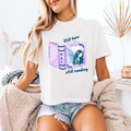 A woman wearing a white boxy crop that reads "still here still reading" with an open book on the front that has a fairy on it
