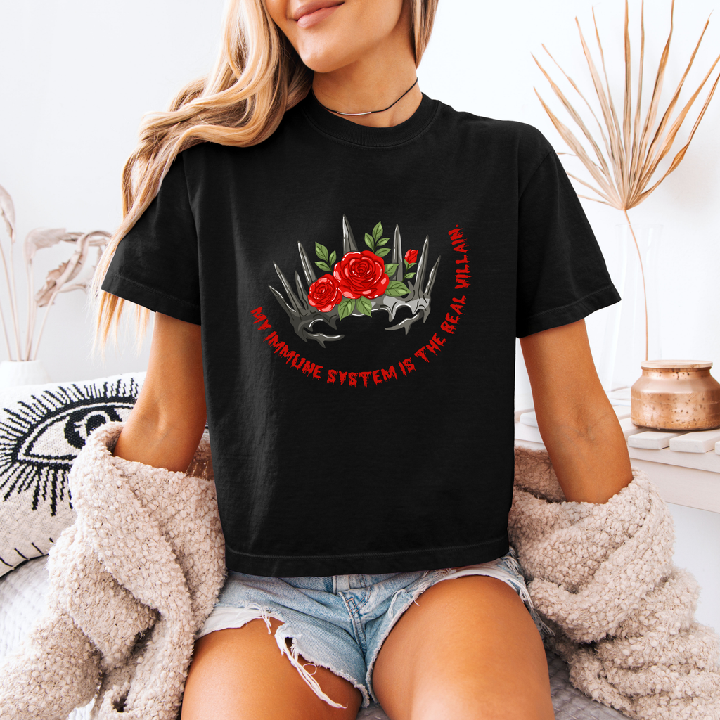 A woman wearing a black boxy crop shirt that has a crown and reads "My immune system is the real villain" 