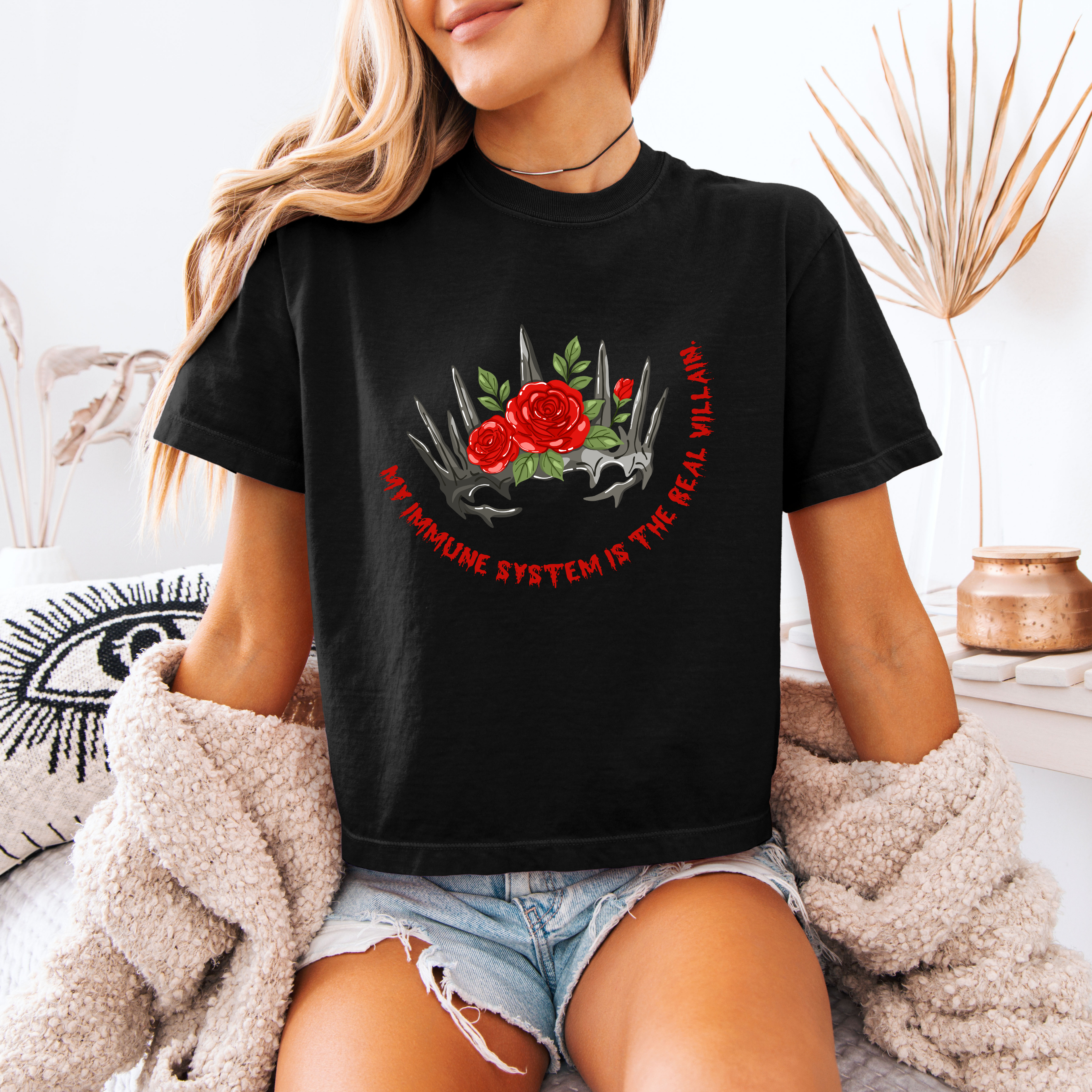 A woman wearing a black boxy crop shirt that has a crown and reads "My immune system is the real villain" 