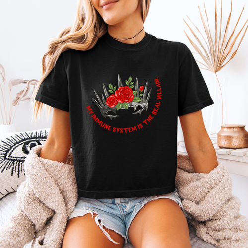 A woman wearing a black boxy crop shirt that has a crown and reads "My immune system is the real villain" 