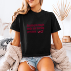 A woman wearing a black boxy crop tee that has a crown and reads "Running on magic, meds and morally grey men"