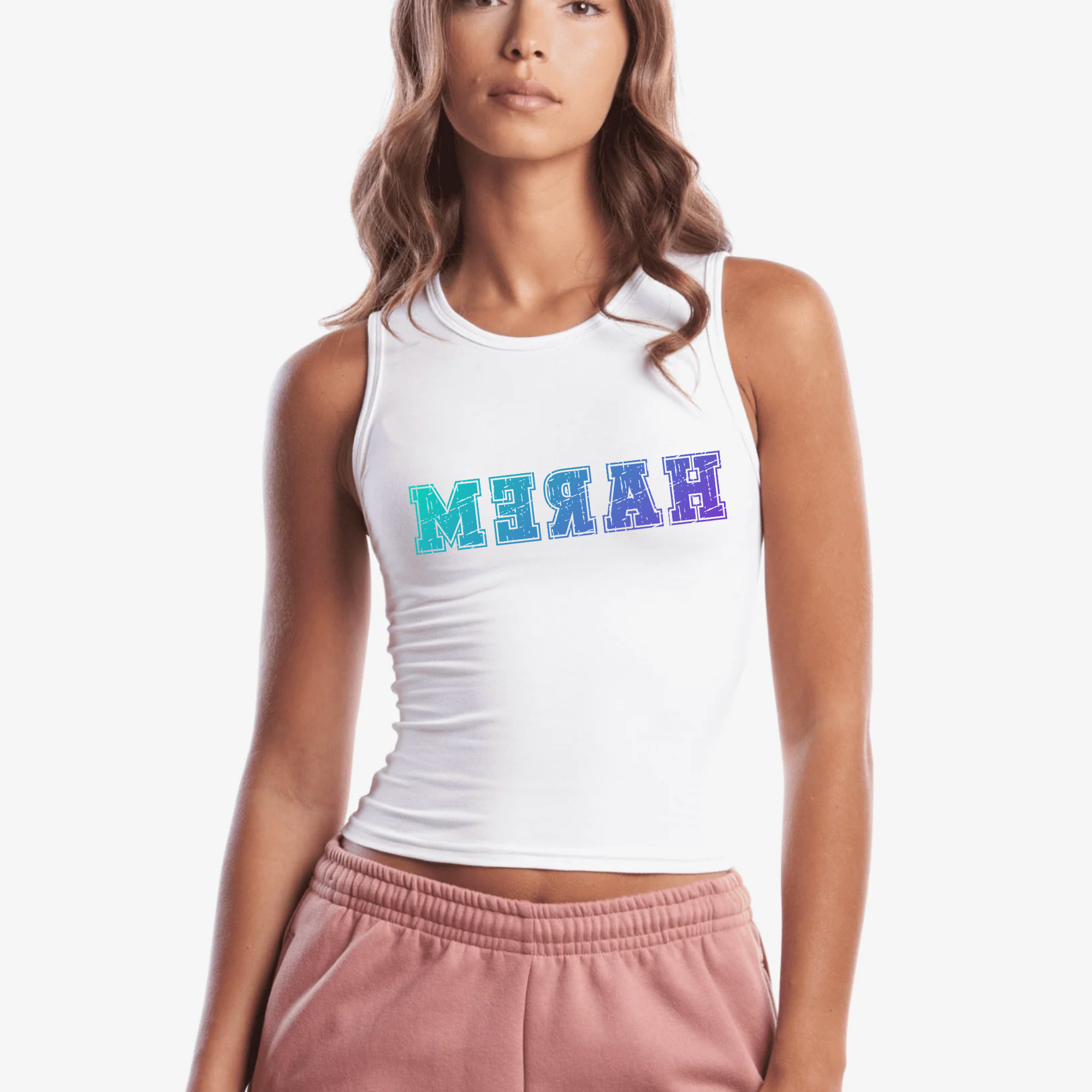 A woman wearing a white sleeveless crop tank top with the 'HAREM' printed across the chest in reverse a blue-to-purple gradient, paired with dusty pink sweatpants, against a plain white background.