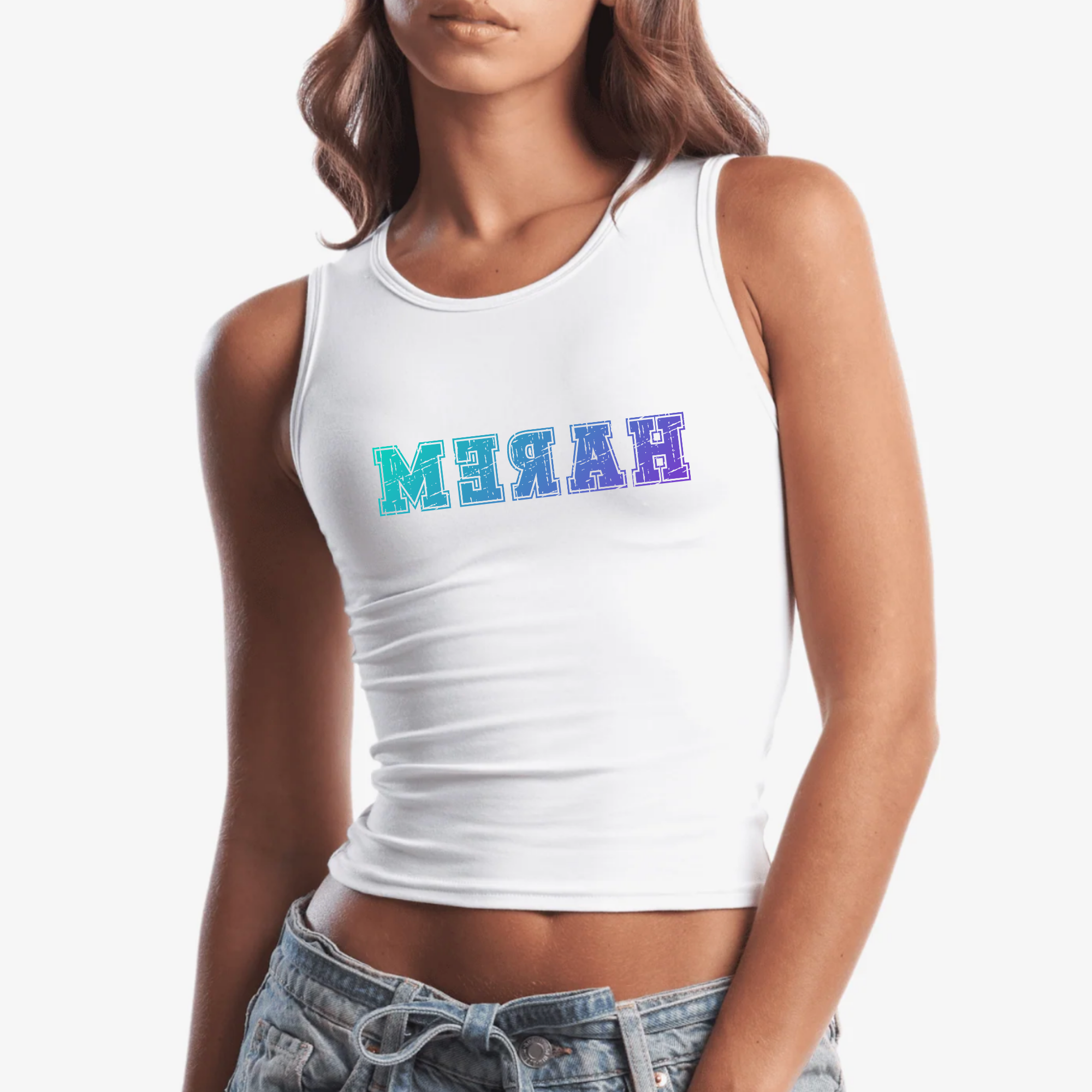 A woman wearing a white sleeveless crop tank top with the word 'HAREM' printed across the chest in reverse in a blue-to-purple gradient. She is also wearing light-wash denim jeans against a plain light gray studio background.