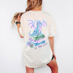 A woman wearing an ivory tee showing the back with a dragon sitting on a stack of books and reads "my tbr isnt"